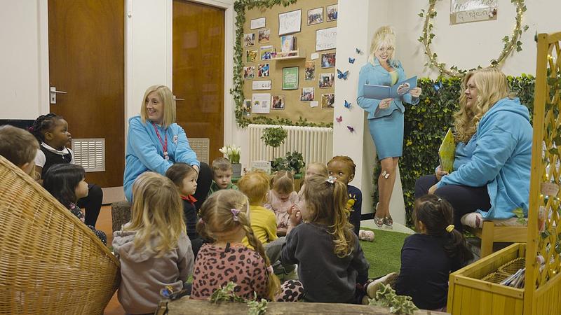 The two learning professional award winners in 2023 gathered on the floor, reading a picture book to children. A life-size cut-out of Dolly Parton is in the background.